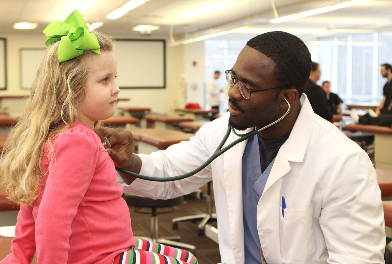 Med student uses stethoscope to listen to girl's heartbeat.