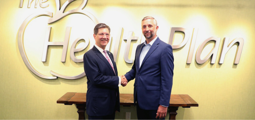 Two men in suits shaking hands in front of a sign that says